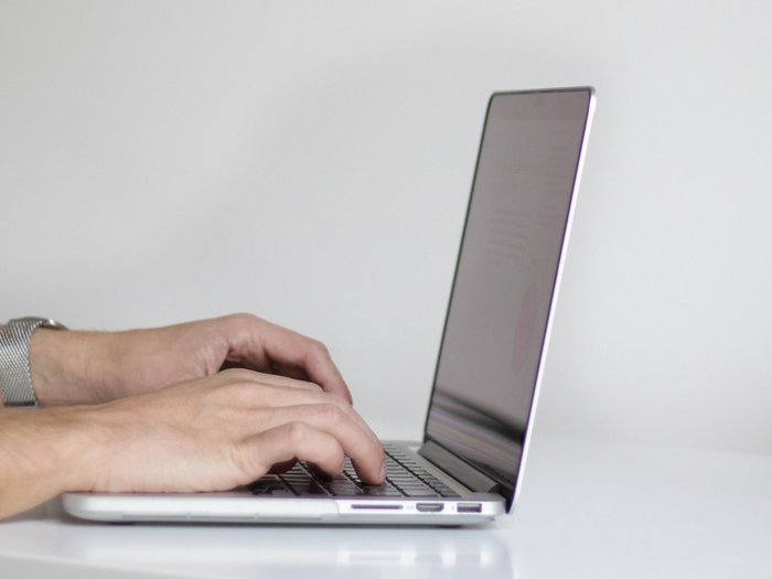 Barrierefreiheit von Webseiten Hände tippen auf Laptop-Tastatur auf weißem Schreibtisch mit Pflanze