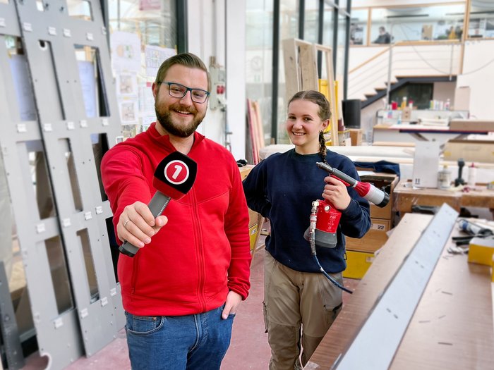 „Zukunft in deiner Hand“ Mann mit Mikrofon interviewt Handwerkerin mit Heißluftpistole in Werkstatt