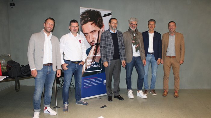 © lvh.apa Sechs Männer stehen vor einer grauen Wand neben einem Werbebanner