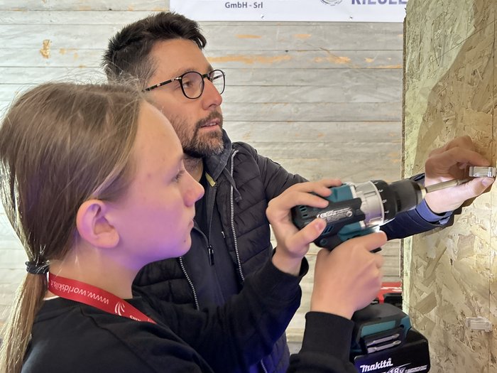 SkillsDay nella Val d'Ega: scoprire l'artigianato, scoprire talenti Donna impara da uomo a usare trapano a batteria durante formazione elettricista