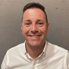 Bruciatoristi Uomo sorridente con capelli corti e camicia bianca davanti a parete grigia