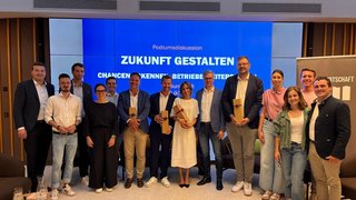News Gruppe von Menschen bei Podiumsdiskussion vor Bildschirm mit Zukunft gestalten