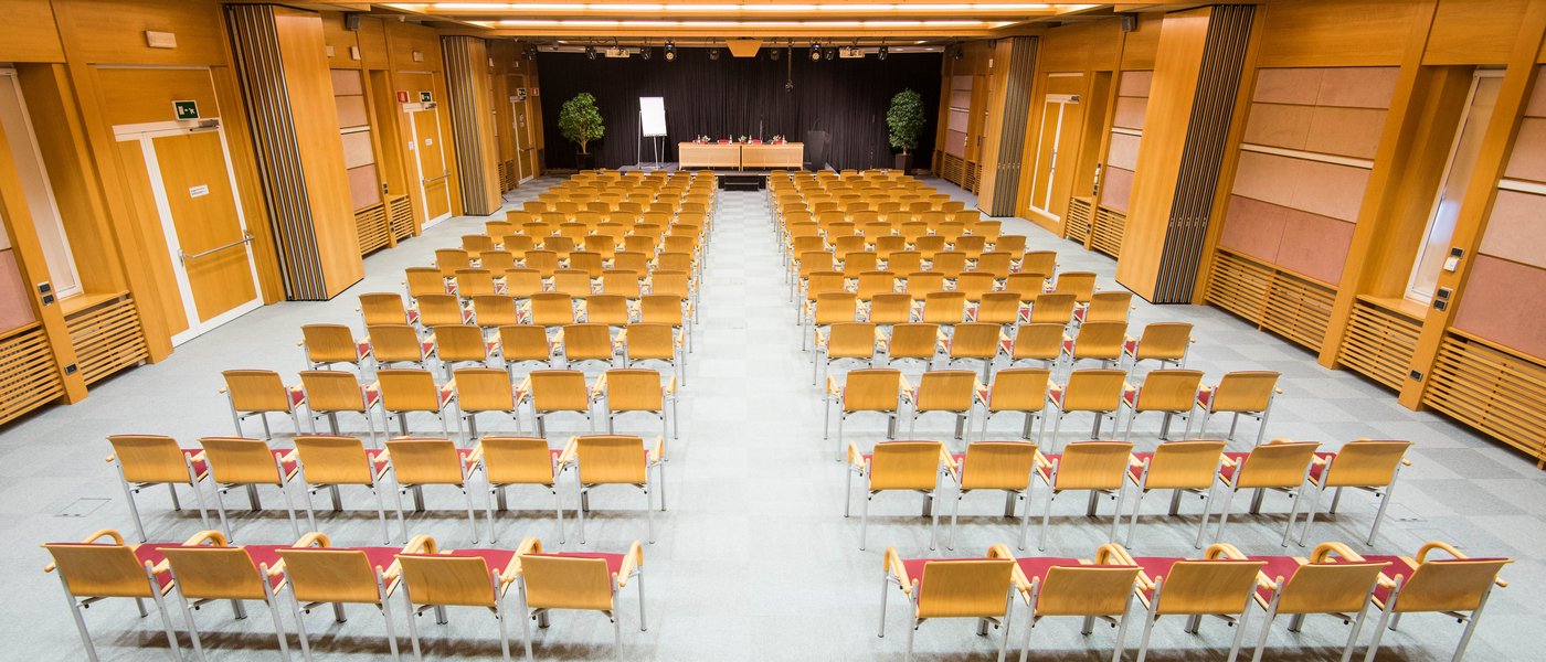 Vermietung Seminarräume Leerer großer Konferenzraum mit mehreren Reihen von Holzstühlen und einem Podium