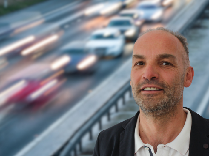 „Verkehrschaos vorprogrammiert“ Mann vor einer vielbefahrenen Straße mit verschwommenem Verkehr im Hintergrund