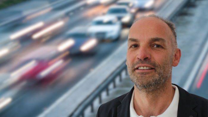 „Verkehrschaos vorprogrammiert“ Mann vor einer vielbefahrenen Straße mit verschwommenem Verkehr im Hintergrund