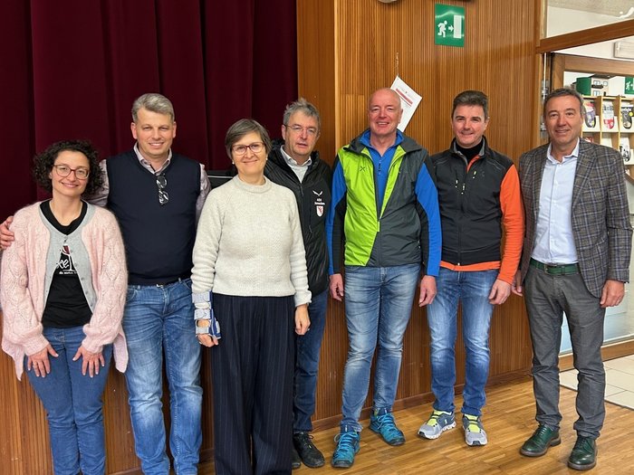 200 Hände am Werk – Tag des Handwerks in Jenesien Sieben Erwachsene stehen in einem Raum vor einer Holzwand mit rotem Vorhang