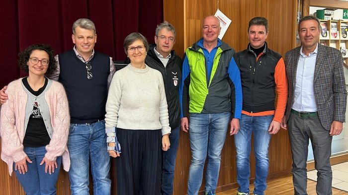 200 mani al lavoro – La Giornata dell’Artigianato a San Genesio Sette adulti in piedi in una stanza davanti a una parete di legno con tenda rossa