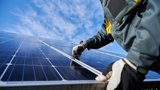 © Shutterstock.com Person repariert oder installiert Solarpanel bei klarem Himmel
