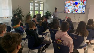 News Schüler im Klassenzimmer schauen Lehrer mit Maske bei Präsentation auf großem Bildschirm zu