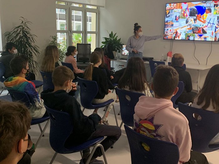 Die Welt der praktischen Berufe Schüler im Klassenzimmer schauen Lehrer mit Maske bei Präsentation auf großem Bildschirm zu