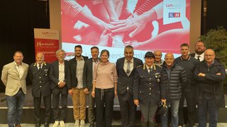 News Gruppenfoto von 13 Personen vor Präsentationsbildschirm bei einer Veranstaltung