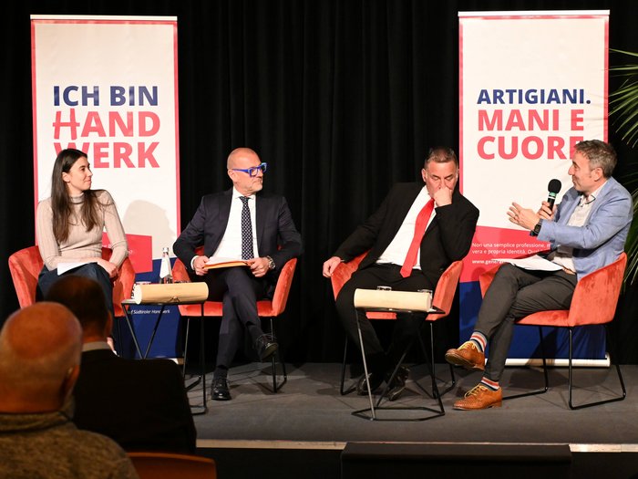 "La città che desideri": un incontro per il futuro di Bolzano Discussione in panel con quattro partecipanti davanti a striscioni su artigianato e mestiere