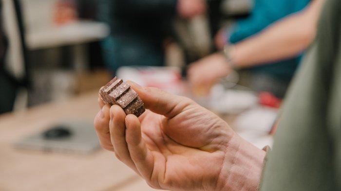 © MakerSpace, lvh.apa, Fiorentino Hand hält kleine, braune geriffelte Schokolade oder Snackstückchen