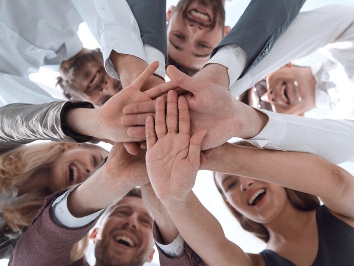 Mitarbeitersuche: Wie Betriebe Fachkräfte finden Gruppe lächelnder Menschen legt Hände zusammen im Teamwork