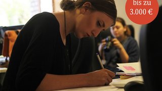 News Junge Frau schreibt konzentriert an einem Tisch im Büro