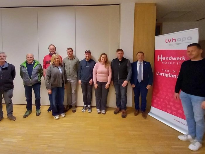 Handwerk und Gemeinde im Dialog: Ortsversammlung in Hafling Eine Gruppe von neun Personen steht vor einer Wand und einem LVH-APA Banner