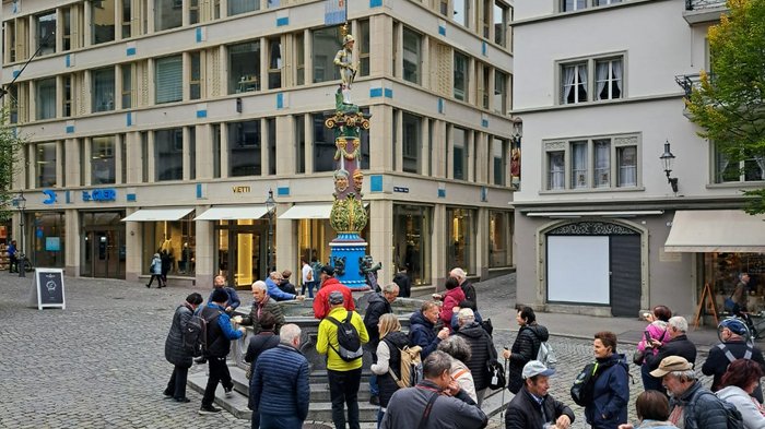 Viaggio autunnale degli artigiani anziani di lvh.apa: puro divertimento e panorama svizzero Persone radunate intorno a una fontana con una statua colorata in una città