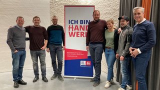 News Gruppe von sieben Personen steht vor Banner mit Schrift Ich bin Handwerker