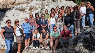 News Foto di gruppo di 27 persone davanti a una parete rocciosa con sole