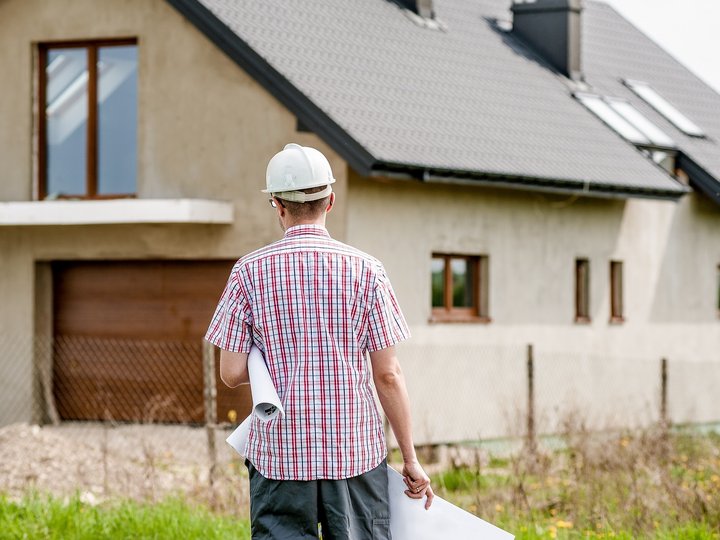 Informationen und Beratungen Bauarbeiter mit Helm und Bauplänen vor einem Haus