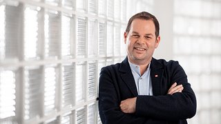 News Mann mit verschränkten Armen vor Glaswand in heller Umgebung