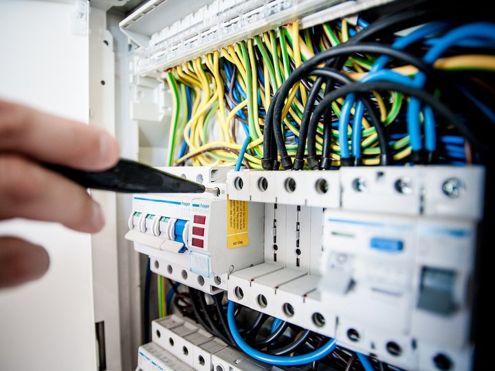 Ausbildung Hand überprüft Sicherungsschalter im Elektrikpanel mit bunten Kabeln
