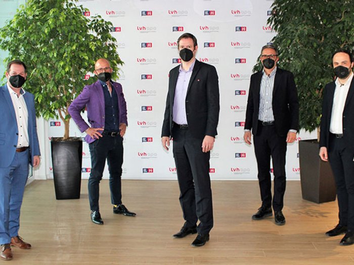 Handwerk: Mit geballter Kraft nach vorne Fünf Männer mit Schutzmasken posieren vor einer Wand mit Firmenlogos