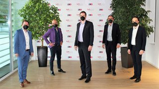 News Fünf Männer mit Schutzmasken posieren vor einer Wand mit Firmenlogos