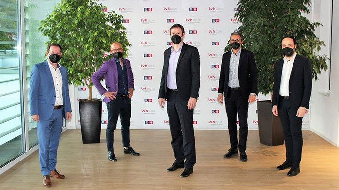 Handwerk: Mit geballter Kraft nach vorne Fünf Männer mit Schutzmasken posieren vor einer Wand mit Firmenlogos