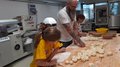 Kids-Academy 2024: Das große Finale Mann mit Kindern formen Teig in einer Bäckerei