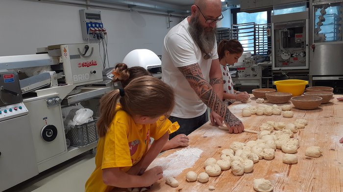 Kids-Academy 2024: Das große Finale Mann mit Kindern formen Teig in einer Bäckerei