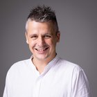 Andrea Zaggia Uomo sorridente con camicia bianca su sfondo grigio