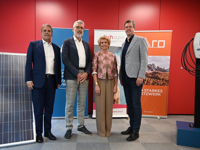 Regionale Allianz für die Energiewende Vier Personen stehen vor einem roten Hintergrund mit Bannern und einem Solarpanel