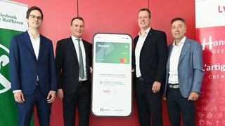 News Quattro uomini in abito presentano un cartellone pubblicitario della carta Renefit Business su sfondo rosso