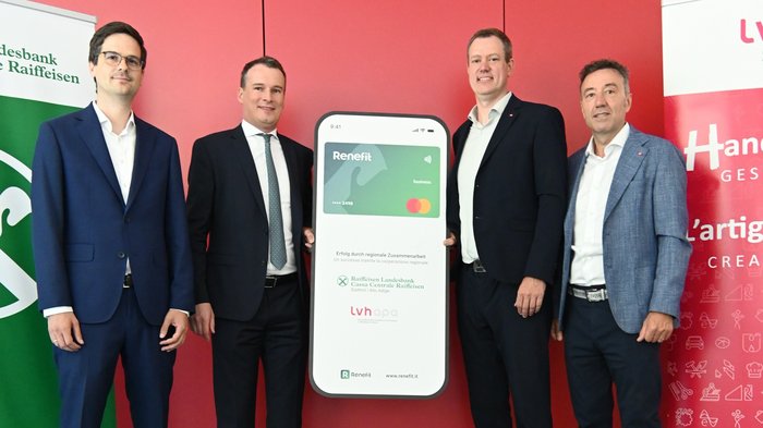 RENEFIT – Digitale Gutscheinkarte zur Mitarbeiterbindung im Handwerk vorgestellt Vier Männer in Anzügen präsentieren Werbetafel für Renefit Businesskarte vor rotem Hintergrund