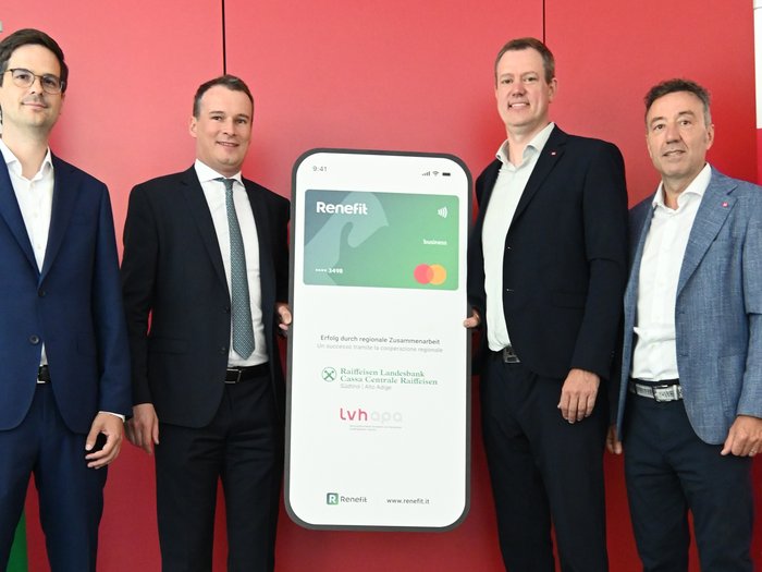 RENEFIT – Digitale Gutscheinkarte zur Mitarbeiterbindung im Handwerk vorgestellt Vier Männer in Anzügen präsentieren Werbetafel für Renefit Businesskarte vor rotem Hintergrund