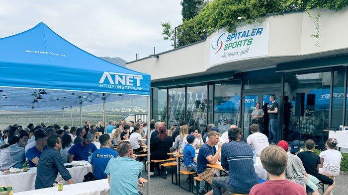 „Anpacken und Gewinnen“ – Eppans erster Handwerksparkour begeistert! Menschenmenge hört bei Sportgeschäft Spitaler Sports Vortrag im Freien unter blauem Zelt zu