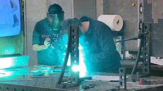 News Zwei Personen schweißen mit Schutzmaske an Metallteile in Werkstatt