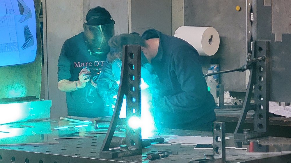 Home Due persone saldano pezzi di metallo con maschera protettiva in officina