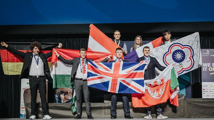 WorldSkills in Bozen: Bronzemedaille und Medallion for Excellence für zwei Südtiroler Siegerteam auf Bühne mit verschiedenen Nationalflaggen bei Preisverleihung