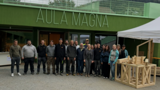 News Gruppenfoto vor Gebäude Aula Magna mit Holzobjekt unter Zelt