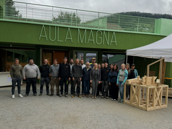 SkillsDay a Vipiteno: l’artigianato da toccare con mano Foto di gruppo davanti all'edificio Aula Magna con oggetto in legno sotto tenda