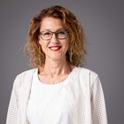 Tiziana Varner Donna sorridente con capelli rossi, occhiali e abito bianco su sfondo grigio