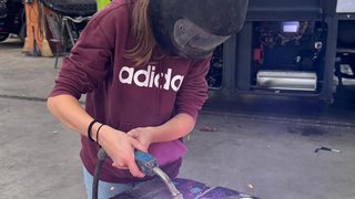 News Person mit Schweißhelm, die in einer Werkstatt Metallteile schweißt