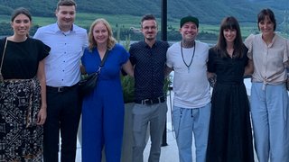 News Sieben Personen stehen Arm in Arm vor einer Berglandschaft