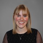 Verena Kofler Ritratto di donna sorridente con capelli biondi e abito nero davanti a sfondo grigio