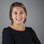 Das lvh-Team Porträt einer lächelnden Frau mit kurzen blonden Haaren und schwarzem Oberteil vor grauem Hintergrund