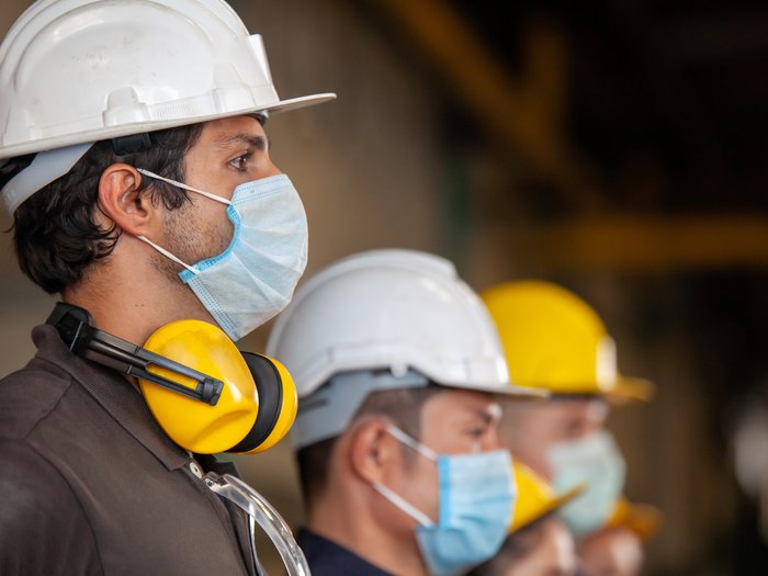 „Eine Herausforderung, die uns zusammenschweißt" Bauarbeiter mit Schutzhelmen und Mundschutz stehen nebeneinander