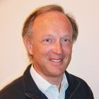 Holzschnitzer Mann mit lockerer Jacke und Hemd lächelt in Kamera vor neutralem Hintergrund