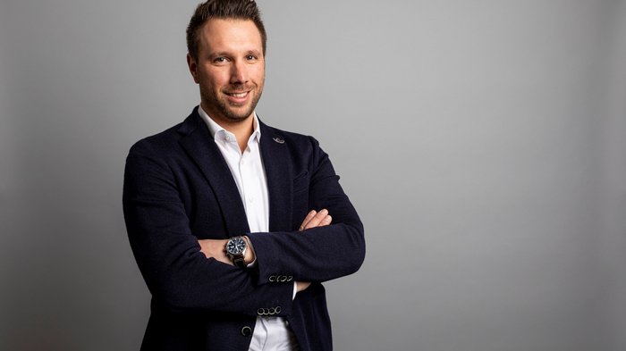 Patente a punti per la sicurezza sul lavoro: un altro onere per le aziende Giovane uomo con giacca elegante davanti a sfondo grigio con le braccia incrociate